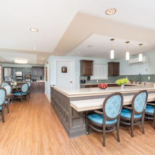 A modern kitchen and dining area with an open layout, featuring wood flooring, bar stools at the counter, and contemporary lighting fixtures.