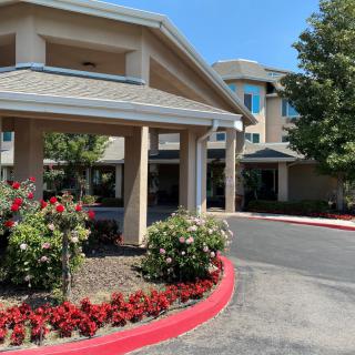 The entrance of a building with landscaped flowers and trees along the driveway.