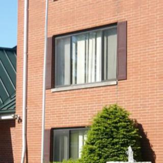 A brick building with windows and a neatly trimmed shrub in front.