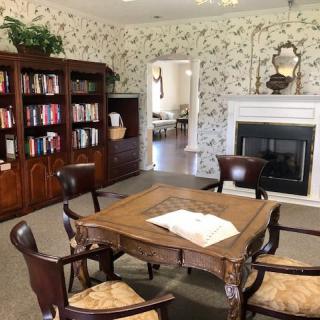 A cozy library room with a wooden table, chairs, bookshelf, and a fireplace.