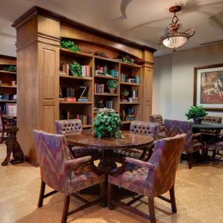 A cozy library setting with bookshelves, a round table, and upholstered chairs.