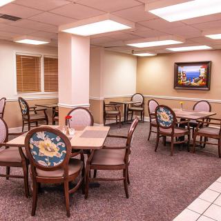 A cozy indoor dining area with multiple tables and chairs, featuring a carpeted floor and artwork on the wall.