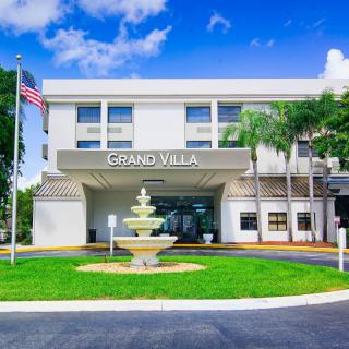 The front view of a building named Grand Villa, featuring a central fountain and surrounded by palm trees.