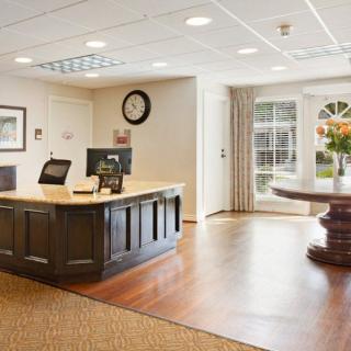 A welcoming office reception area featuring a large desk with a computer, wall clock, and bright natural light from the windows.