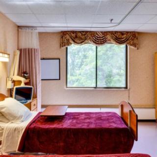 A hospital room featuring a bed, television, and window with curtains.