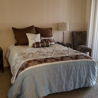 A cozy bedroom featuring a neatly made bed with pillows and a decorative blanket, accompanied by a lamp and chair.