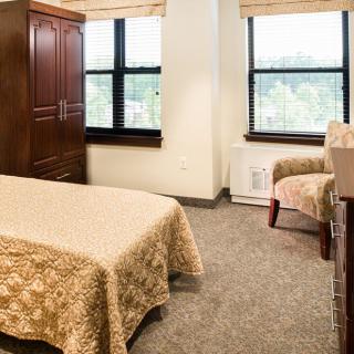 A cozy bedroom with a single bed, wardrobe, and armchair, featuring two large windows.