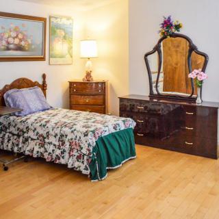 A cozy bedroom featuring traditional furnishings, including a single bed and a dresser with a mirror.