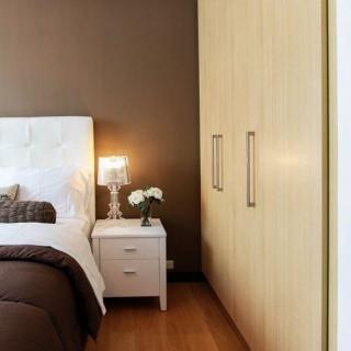A cozy bedroom featuring a neatly arranged bed, a nightstand with a lamp and flowers, and a built-in wardrobe.