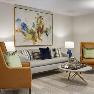 A modern living room featuring a gray sofa, two brown armchairs, a stylish coffee table, and a large abstract painting on the wall.