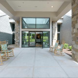 Modern building entrance with glass doors and rocking chairs.
