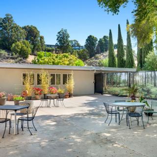 A sunny outdoor patio featuring tables and chairs surrounded by a landscaped garden and modern architecture.