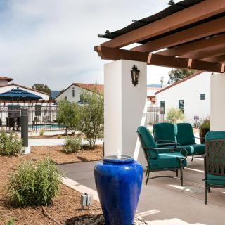 A serene outdoor patio with comfortable seating and a blue vase under a pergola, surrounded by well-maintained landscaping.