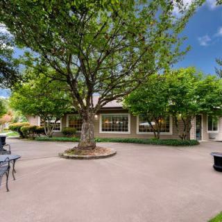 A tranquil outdoor patio area with benches, surrounded by lush trees and a charming house in the background.