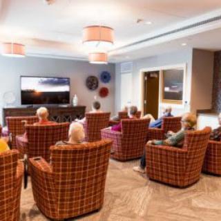 A group of seniors enjoying a communal television viewing in a comfortable lounge setting.