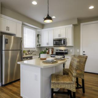 A modern kitchen featuring white cabinets, an island with bar stools, and stainless steel appliances.