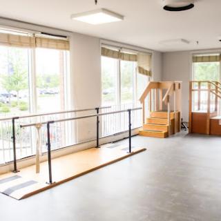 A spacious physical therapy room equipped with walking rails and stairs for rehabilitation exercises.
