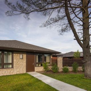 A single-story house with a neatly trimmed lawn and a large tree in the front yard.