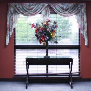 A decorative table with a bouquet of colorful flowers in front of a large window with curtains.