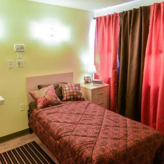 A cozy bedroom with a single bed, warm lighting, and red curtains.