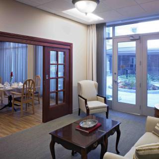 A cozy living room with a view into the dining area, featuring traditional furniture and glass doors leading outside.