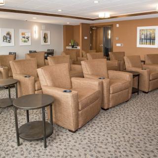 A cozy theater room with rows of beige recliners and side tables, featuring a warm interior design.