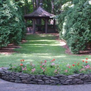 A peaceful garden scene featuring a stone flower bed and a gazebo surrounded by lush greenery.