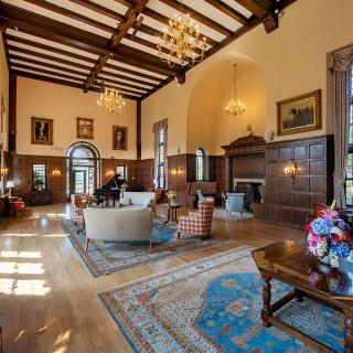 A luxurious and elegant living room with high ceilings, wooden beams, chandeliers, and classic furniture.
