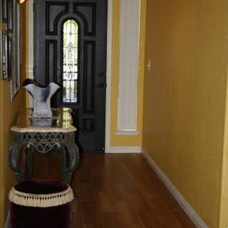 A hallway with yellow walls, featuring a small table adorned with a vase, and a door at the end.