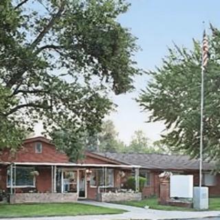 A suburban brick house with a well-maintained lawn and tall trees surrounding it, featuring a flagpole in the front yard.