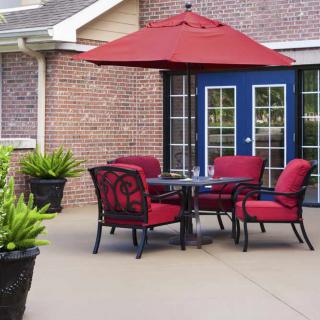 A cozy outdoor patio setup featuring red cushioned chairs and a matching umbrella, set against a brick wall with French doors.
