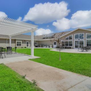 A spacious outdoor area with a pergola and seating, adjacent to a modern building under a partly cloudy sky.