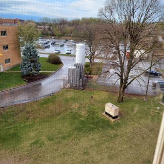 A view of the landscape featuring trees, a building, and a parking area under a cloudy sky.
