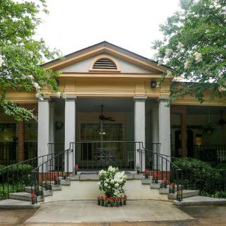A welcoming front entrance of a house, featuring elegant columns and a flower pot surrounded by greenery.