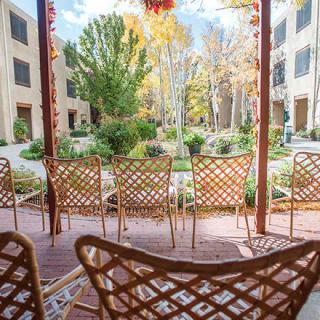 A cozy patio with lattice chairs overlooks a serene garden with trees and a building in the background, capturing an autumnal atmosphere.