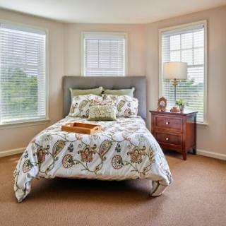 A cozy bedroom featuring a neatly made bed with patterned bedding, natural light streaming in through multiple windows, and stylish furniture.