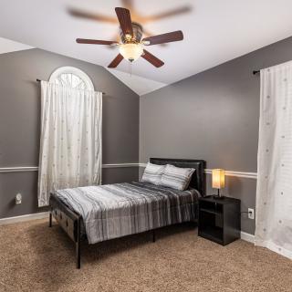 A modern bedroom featuring a neatly made bed, soft carpet flooring, and stylish decor with a ceiling fan above.