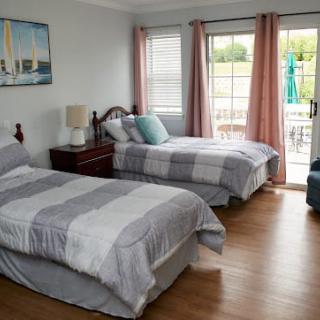 A cozy bedroom with two twin beds, featuring natural light from large windows and wooden flooring.