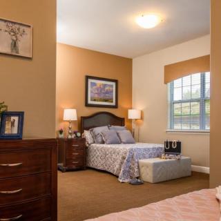 A well-decorated bedroom with warm tones, featuring a bed, nightstands with lamps, and a large window.