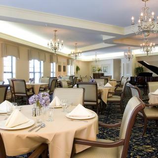 An elegant dining room with neatly arranged tables, chandeliers, and a grand piano.