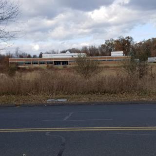 An abandoned building surrounded by overgrown vegetation under a cloudy sky.
