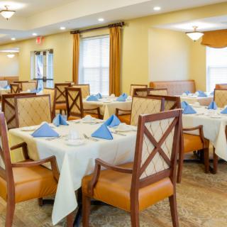 An elegantly set dining room with tables and chairs arranged neatly, featuring blue napkins and warm lighting.