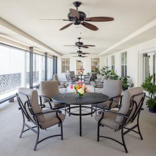 A spacious covered patio featuring a dining set and ceiling fans, with plants enhancing the relaxing atmosphere.