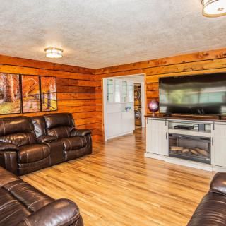 A cozy living room featuring leather couches, wood paneling, a large TV above a fireplace, and hardwood flooring.
