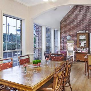 A cozy dining area with wooden furniture, large windows, and a brick accent wall.