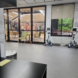 A spacious indoor area featuring modern furniture and exercise equipment, with large windows allowing natural light.