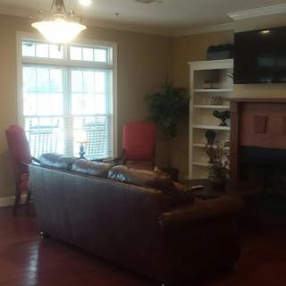 A cozy living room featuring a sofa, large window, shelves, and a fireplace with a television mounted above.
