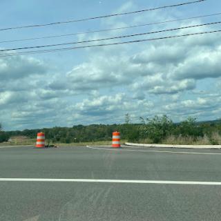 A view of a road under construction, marked by orange traffic cones and a cloudy sky.