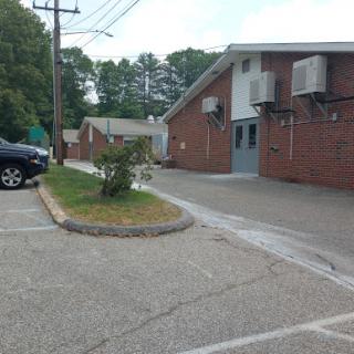A view of a brick building with air conditioning units, surrounded by a parking lot and greenery.