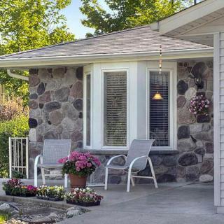 A cozy porch with chairs and flowers in front of a stone-walled house.